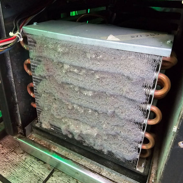 Close-up of a dirty condenser coil with copper fins inside an industrial setting.
